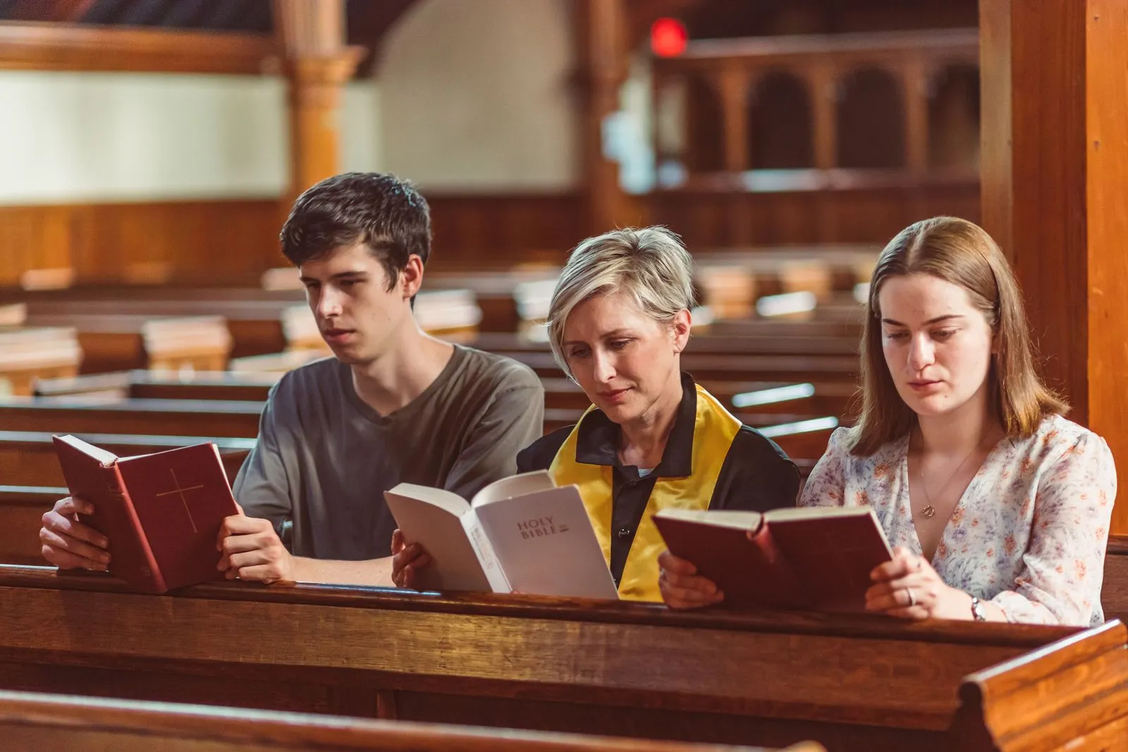 Three people reading bibles together pews